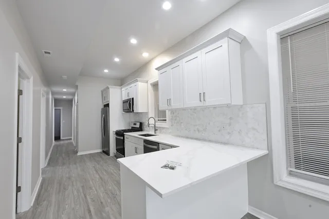a view of a kitchen with kitchen island a sink wooden floor and stainless steel appliances