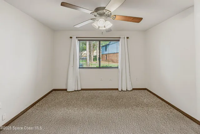 an empty room with a chandelier fan and a wooden floor