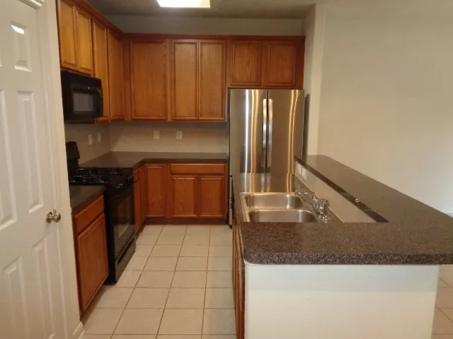 a kitchen with stainless steel appliances granite countertop a refrigerator a stove and a sink with wooden cabinets