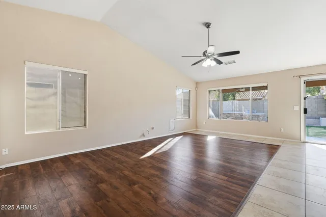 an empty room with wooden floor chandelier fan and windows