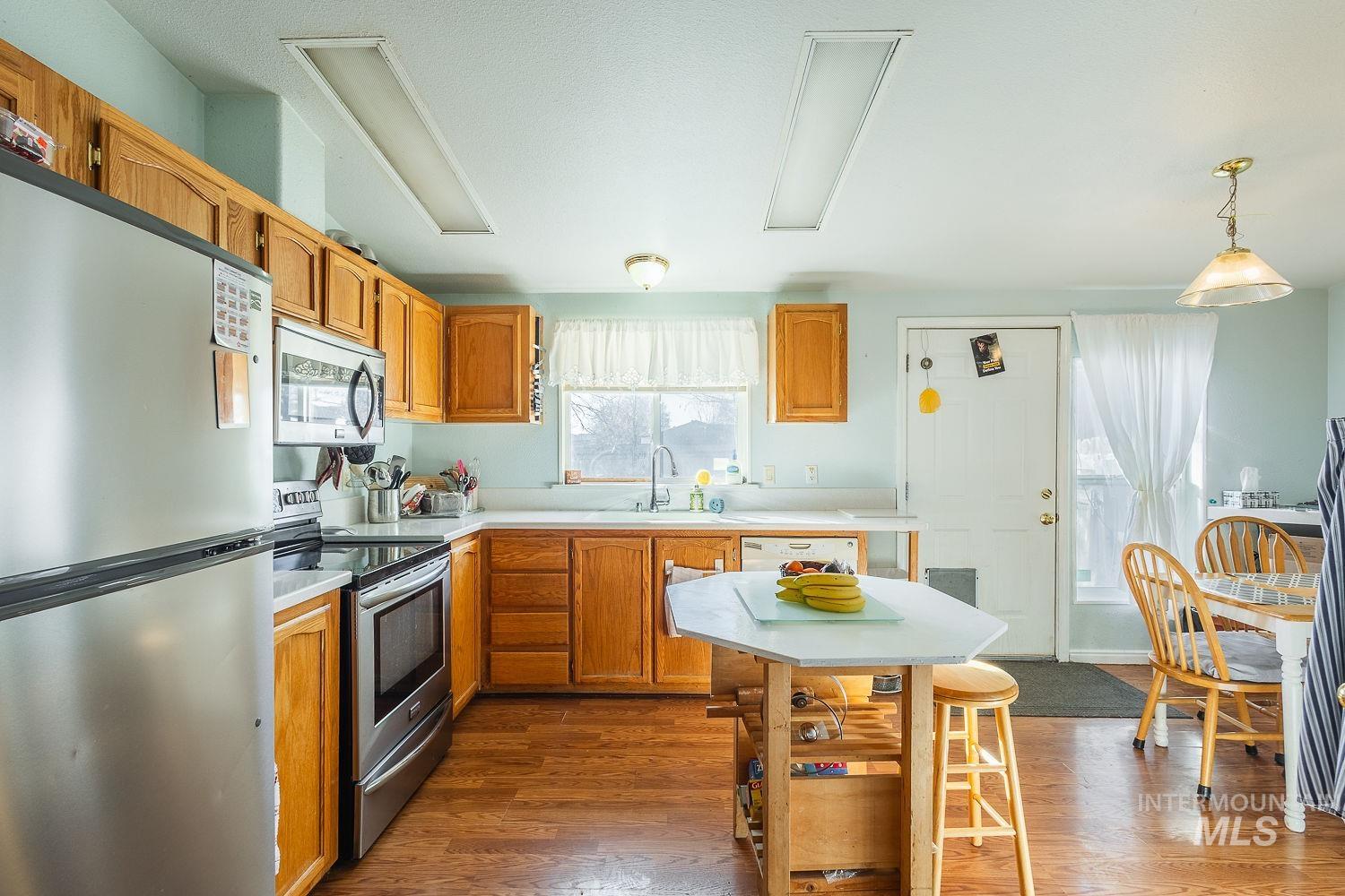 4119 Ashton Avenue Caldwell, ID 83607 - Photo 13 of 50 Kitchen featuring stainless steel appliances, light countertops, wood finish cabinets, dark wood-style flooring, and pendant lighting