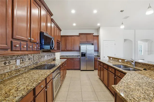 a large kitchen with stainless steel appliances granite countertop a stove a sink and a wooden cabinets