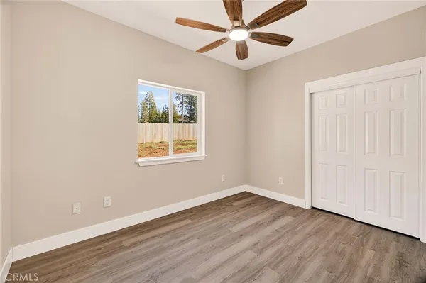an empty room with wooden floor chandelier fan and windows