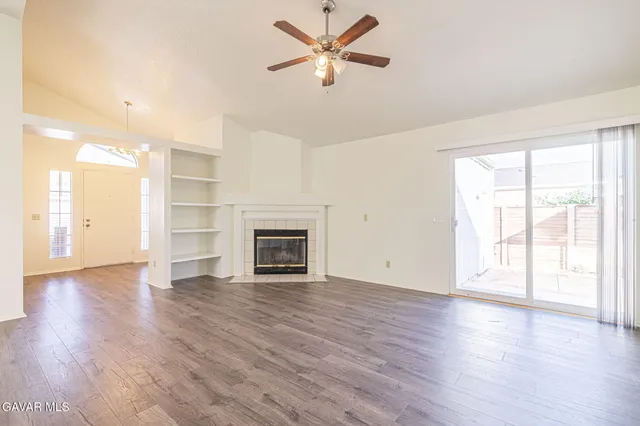 an empty room with wooden floor a ceiling fan a fireplace and windows
