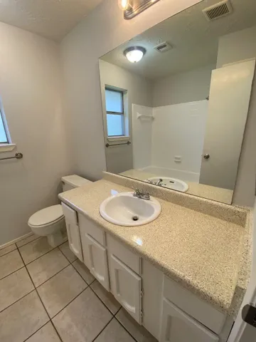 a spacious bathroom with a granite countertop sink a toilet a mirror and shower