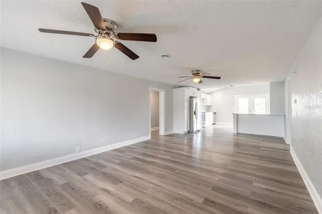 a view of an empty room with wooden floor and a ceiling fan