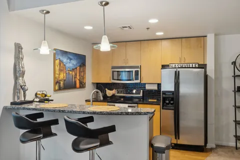 a kitchen with stainless steel appliances granite countertop a sink a stove a refrigerator cabinets and chairs