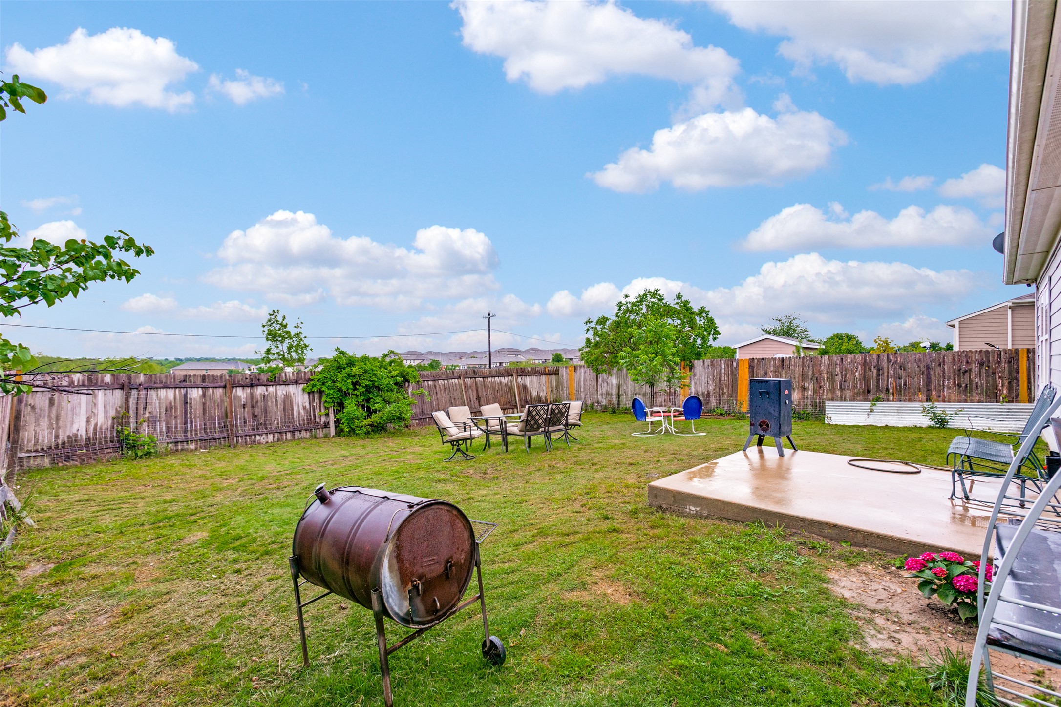 13909 Sherri Berry Way Manor, TX 78653 - Photo 21 of 28 Spacious backyard featuring a substantial concrete patio, expansive lawn area, full perimeter wood fencing, and mature trees