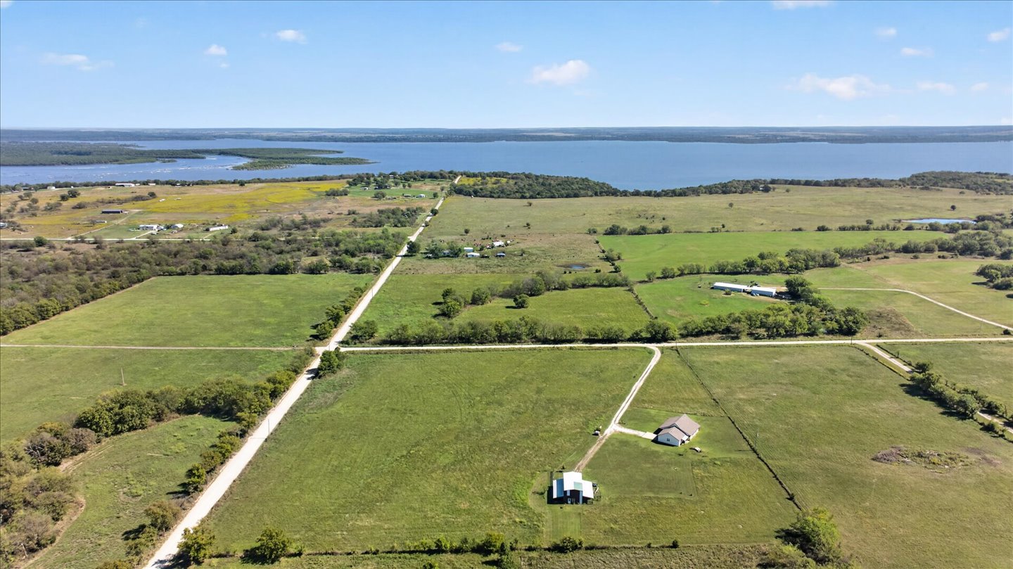 26115 4157th Road Nowata, OK 74048 - Photo 34 of 36 Expansive green fields with a visible body of water in the background, featuring scattered trees and a clear sky