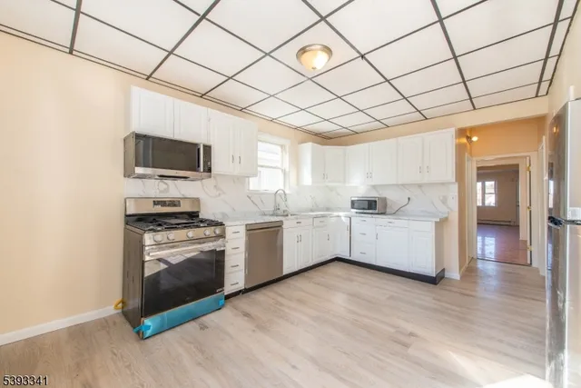 a kitchen with stainless steel appliances kitchen island granite countertop a stove a sink and white cabinets with wooden floor