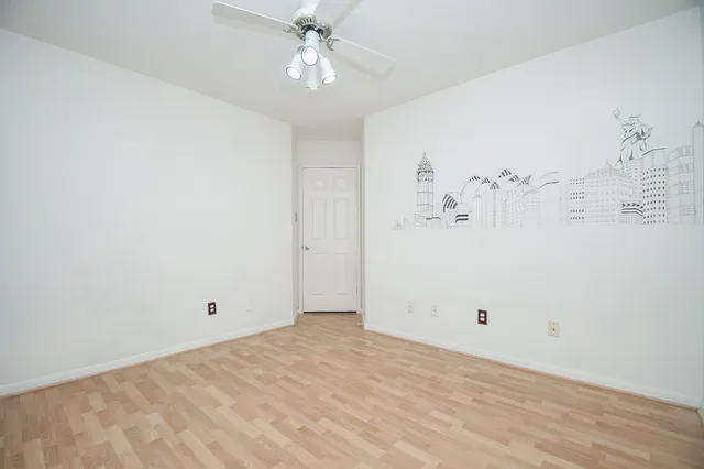 an empty room with a chandelier fan and wooden floor