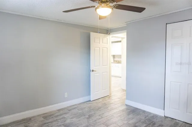 an empty room with a chandelier fan and wooden floor