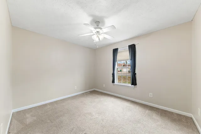 an empty room with chandelier fan and windows