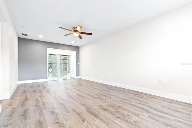 an empty room with wooden floor ceiling fan and windows