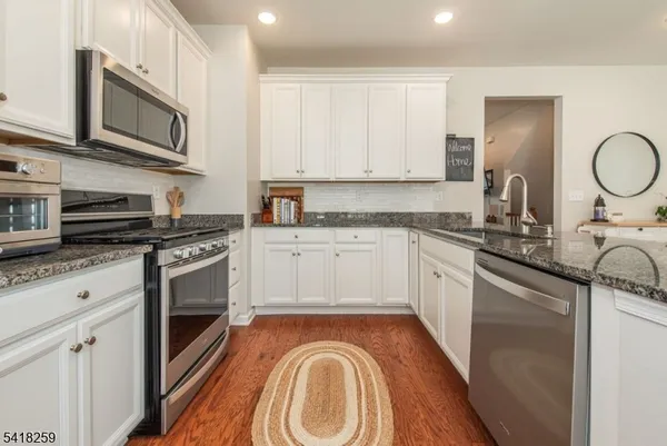 a kitchen with stainless steel appliances granite countertop a stove a sink dishwasher and a microwave oven with white cabinets