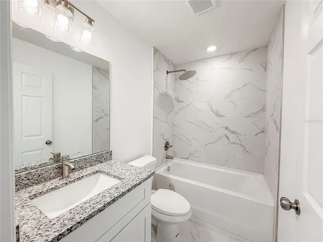 a bathroom with a granite countertop sink toilet mirror and bathtub