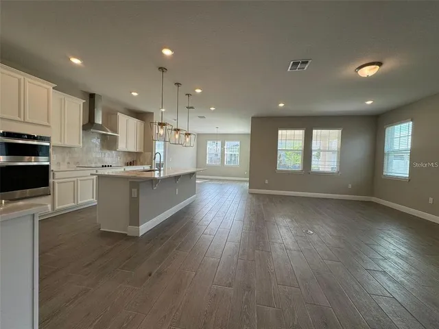 a kitchen with stainless steel appliances granite countertop a stove top oven a sink and white cabinets with wooden floor