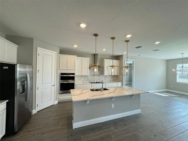a room with stainless steel appliances kitchen island granite countertop a refrigerator and a sink