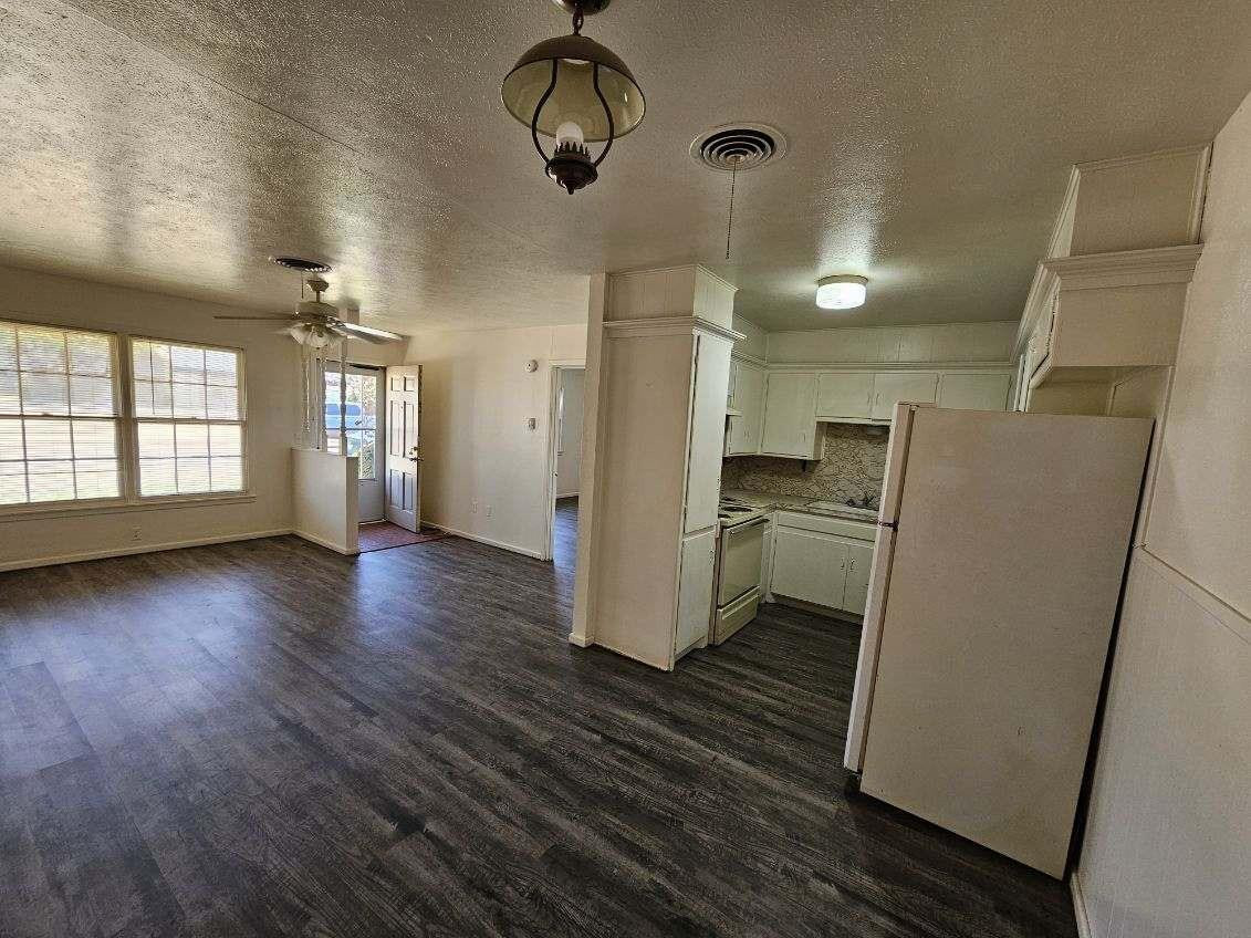 4201 50th Street, Unit A Lubbock, TX 79413 - Photo 4 of 7 an empty room with wooden floor and a kitchen