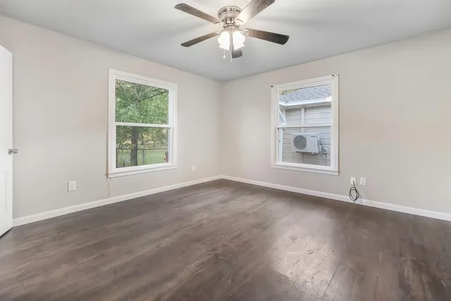 an empty room with wooden floor chandelier fan and windows