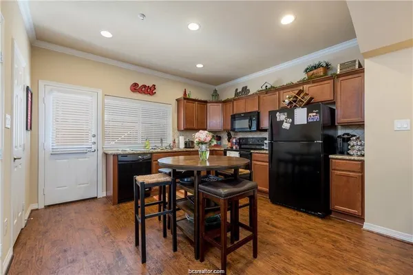 a kitchen with stainless steel appliances kitchen island granite countertop a refrigerator a stove a sink a dining table and chairs with wooden floor