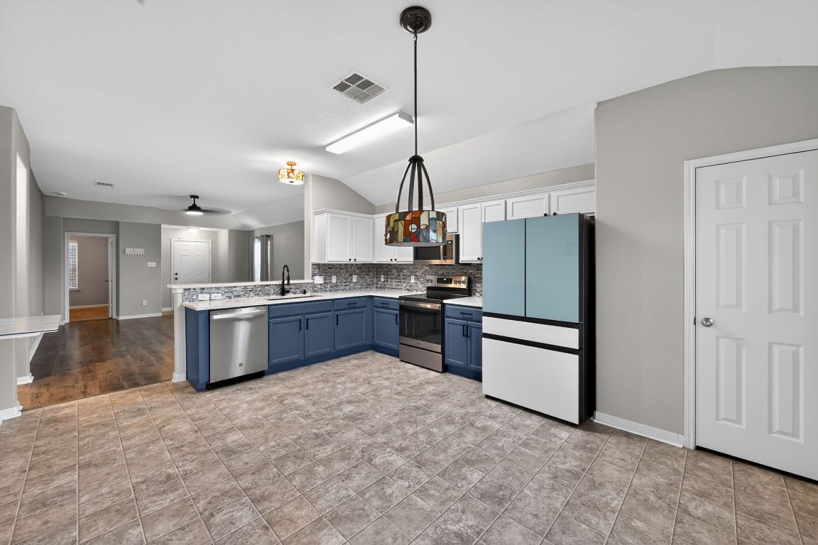 13237 Pine Needle Street Manor, TX 78653 - Photo 5 of 16 Kitchen featuring lofted ceiling, appliances with stainless steel finishes, light countertops, white cabinetry, and blue cabinetry