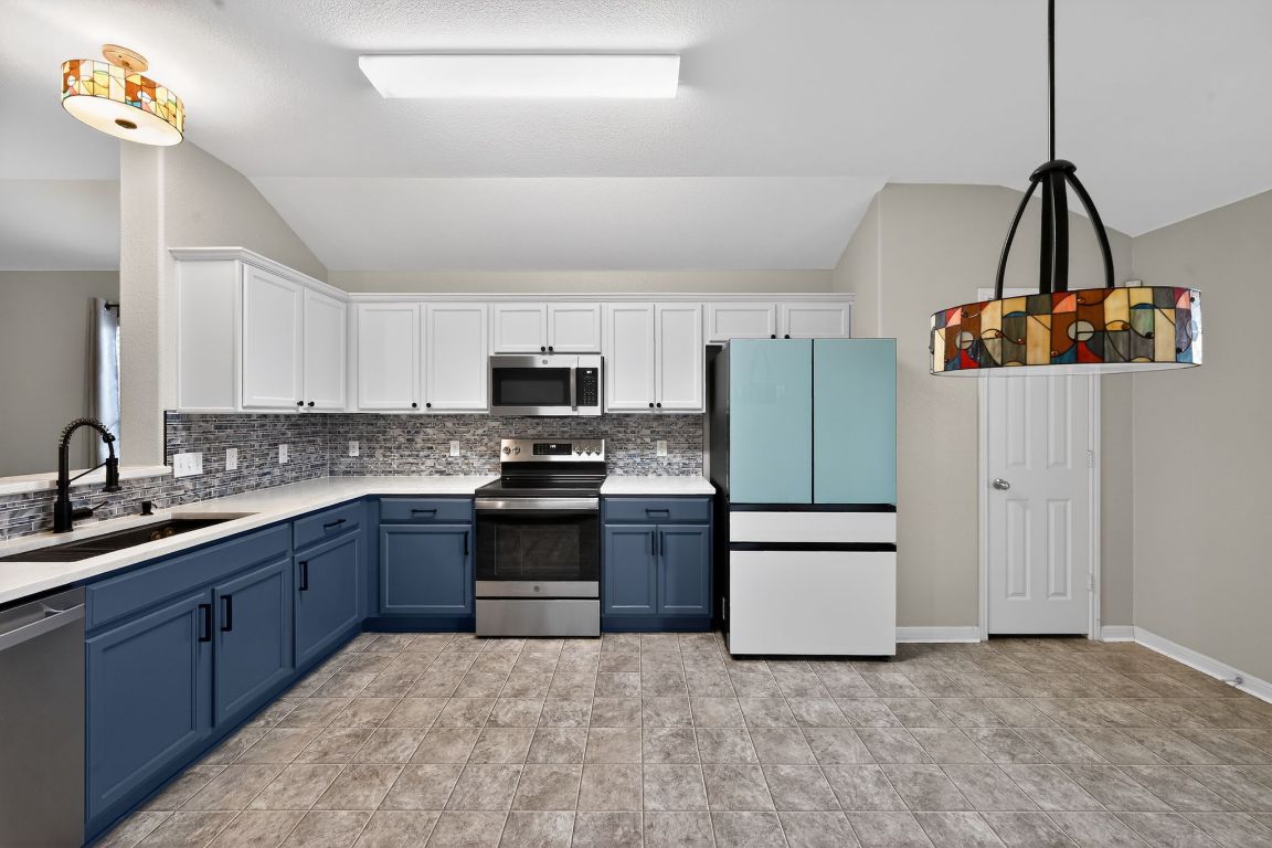 13237 Pine Needle Street Manor, TX 78653 - Photo 6 of 16 Kitchen with white cabinetry, blue cabinetry, appliances with stainless steel finishes, decorative light fixtures, and backsplash