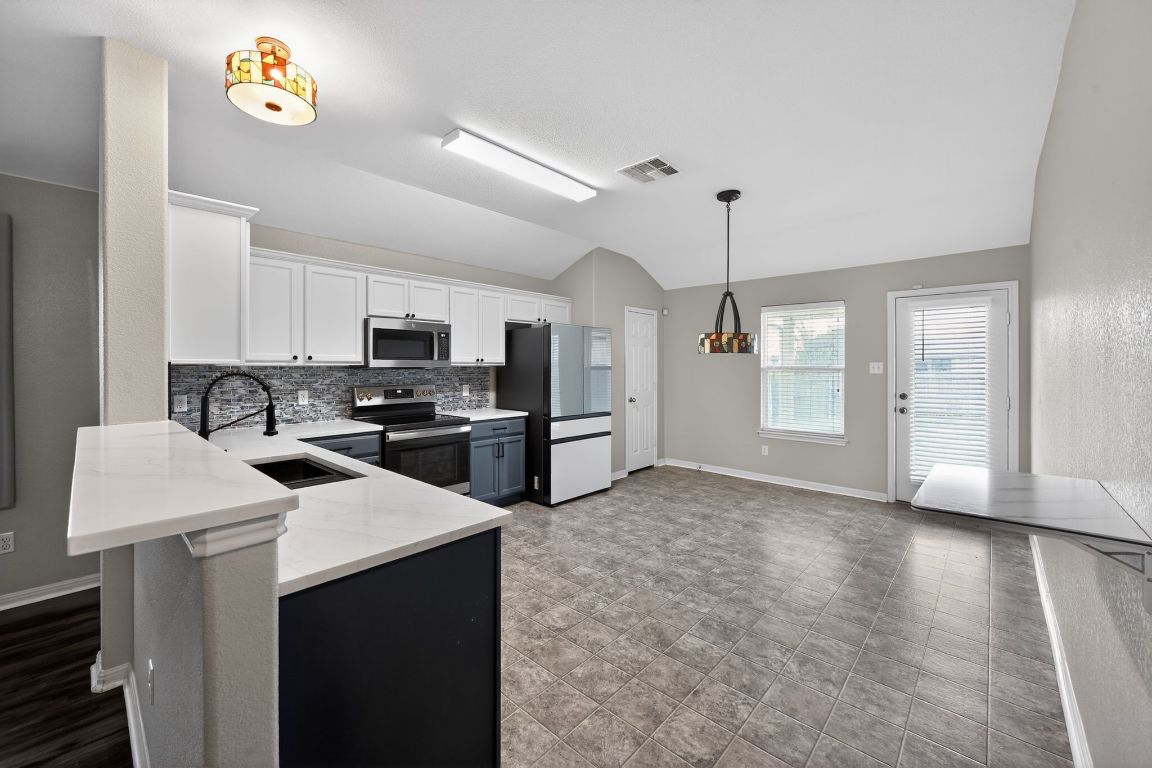 13237 Pine Needle Street Manor, TX 78653 - Photo 7 of 16 Kitchen with stainless steel appliances, white cabinetry, vaulted ceiling, pendant lighting, and tasteful backsplash