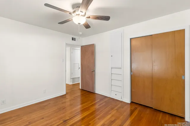 an empty room with wooden floor closet fan and windows
