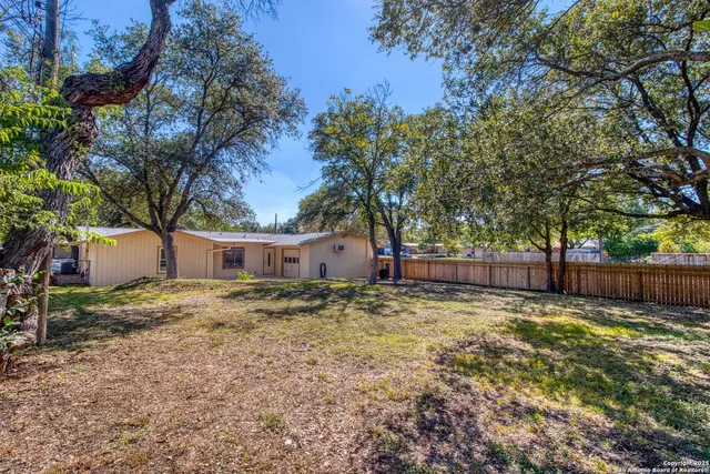 a backyard of a house with large trees and wooden fence