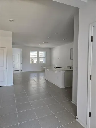 a view of an empty room with kitchen and window
