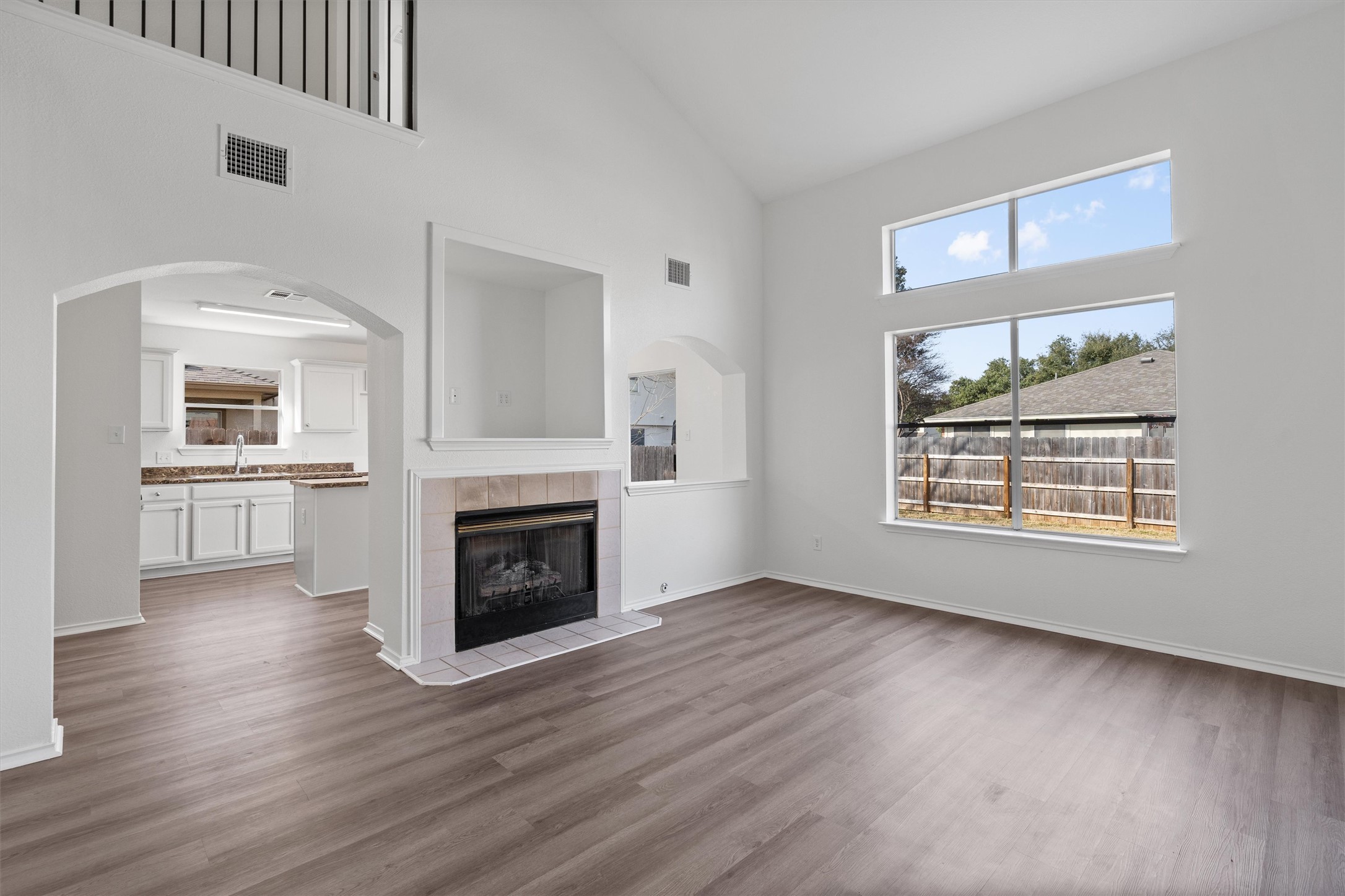 2101 Jester Farms Road Round Rock, TX 78664 - Photo 3 of 24 Unfurnished living room with arched walkways, high vaulted ceiling, a tiled fireplace, and dark wood finished floors