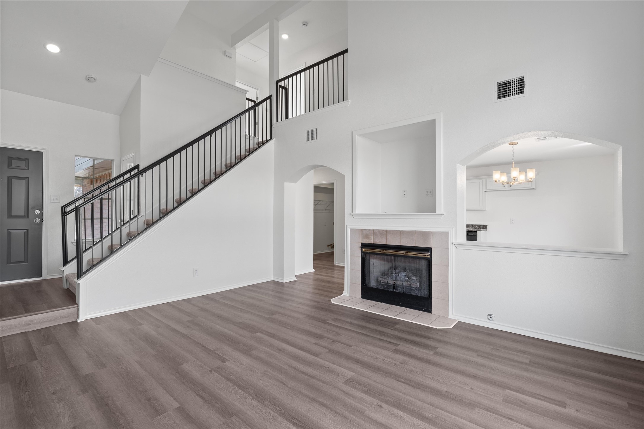 2101 Jester Farms Road Round Rock, TX 78664 - Photo 6 of 24 Unfurnished living room featuring arched walkways, a high ceiling, a fireplace, wood finished floors, and stairway