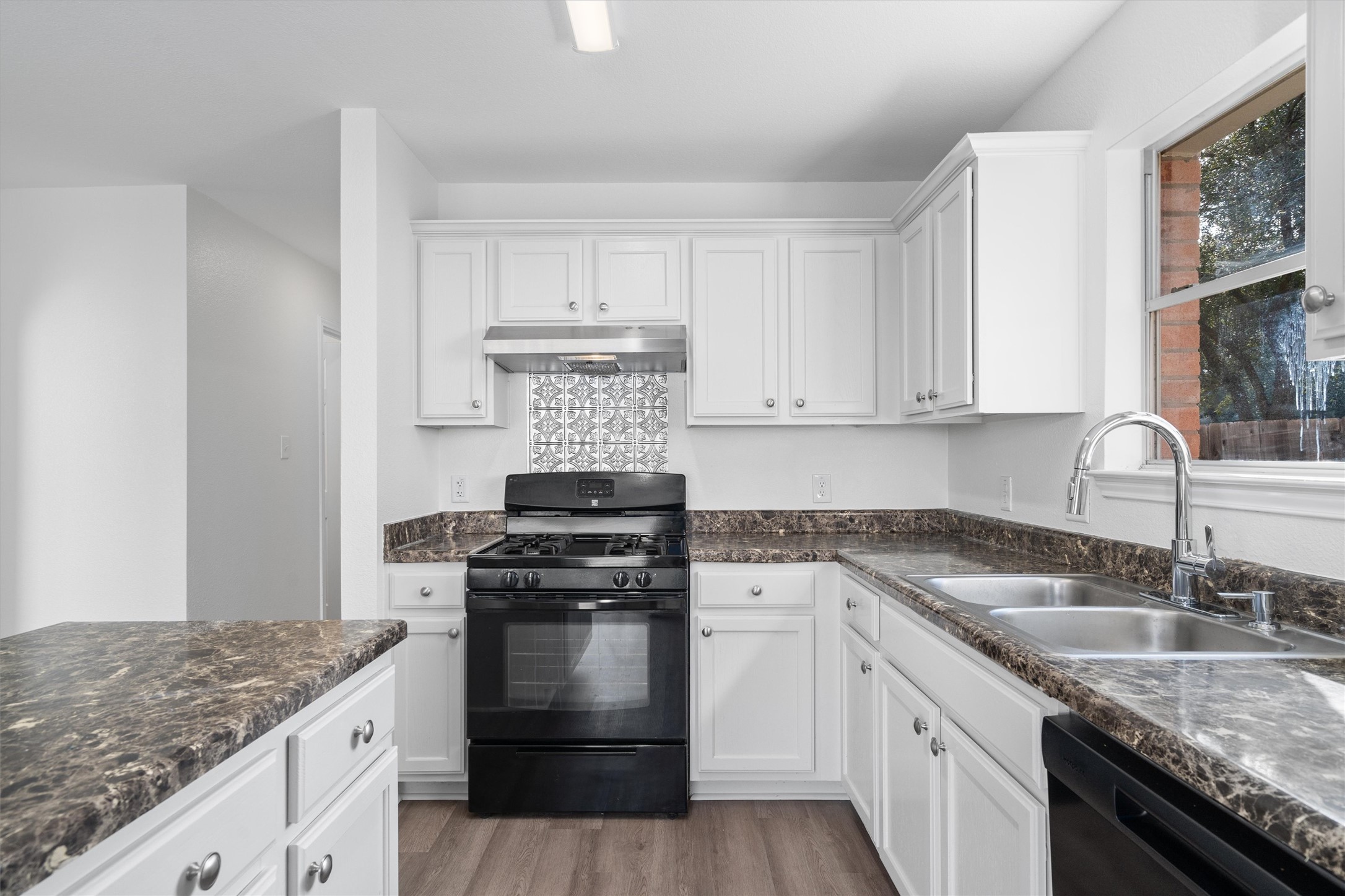 2101 Jester Farms Road Round Rock, TX 78664 - Photo 10 of 24 Kitchen featuring black appliances, white cabinets, under cabinet range hood, light wood-style floors, and dark stone countertops