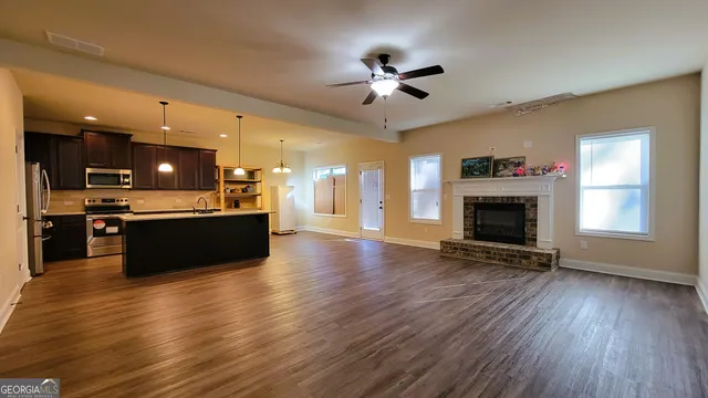 a view of a livingroom with a fireplace a ceiling fan and a kitchen