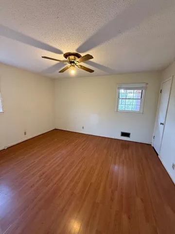 an empty room with wooden floor fan and windows