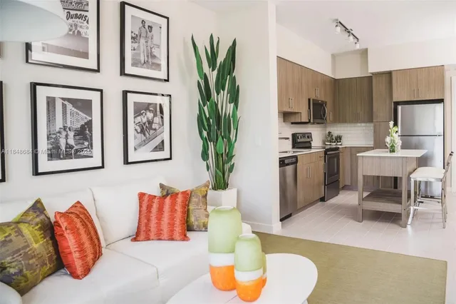 a living room with stainless steel appliances furniture a potted plant and a kitchen view