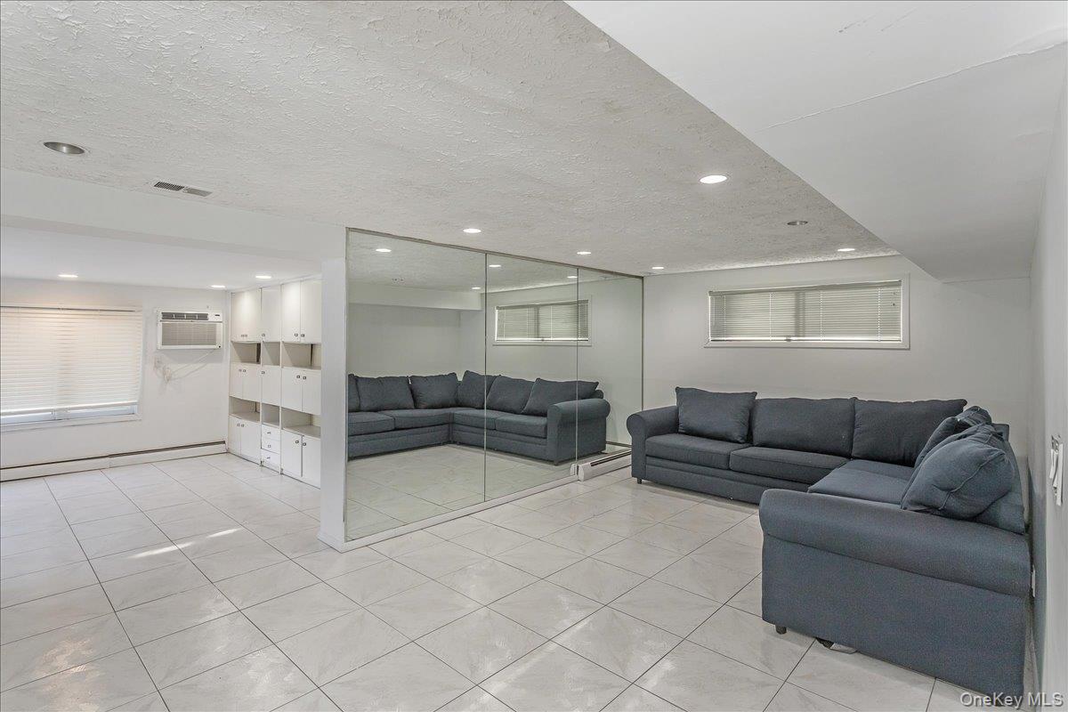 93 Searingtown Road Albertson, NY 11507 - Photo 15 of 24 Living area with a textured ceiling, light tile patterned flooring, a baseboard radiator, and a wall mounted air conditioner