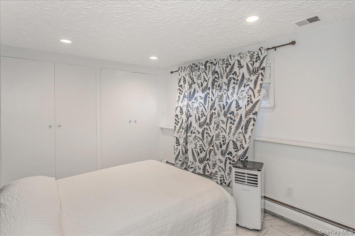 93 Searingtown Road Albertson, NY 11507 - Photo 18 of 24 Bedroom featuring a baseboard radiator, a textured ceiling, two closets, recessed lighting, and marble finish flooring