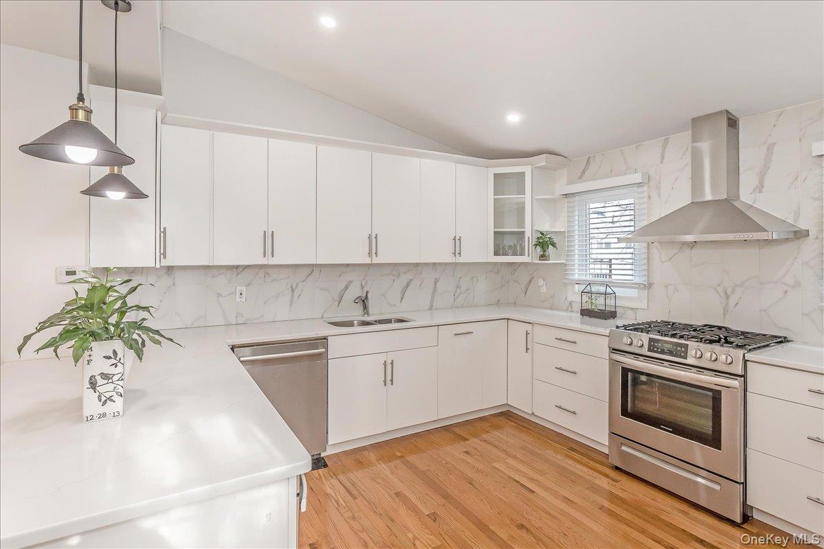 93 Searingtown Road Albertson, NY 11507 - Photo 4 of 24 Kitchen with stainless steel appliances, wall chimney range hood, decorative light fixtures, vaulted ceiling, and white cabinets