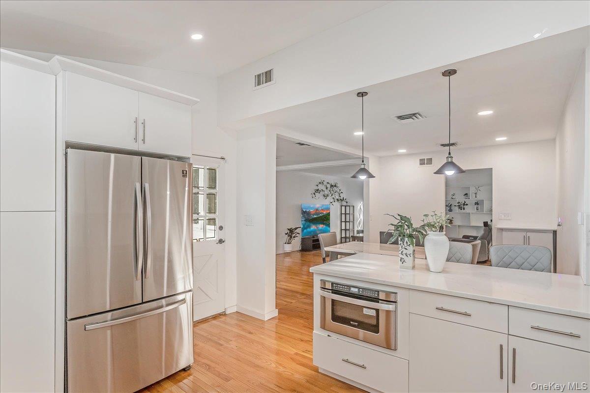 93 Searingtown Road Albertson, NY 11507 - Photo 6 of 24 Kitchen featuring appliances with stainless steel finishes, white cabinets, hanging light fixtures, recessed lighting, and light wood-type flooring