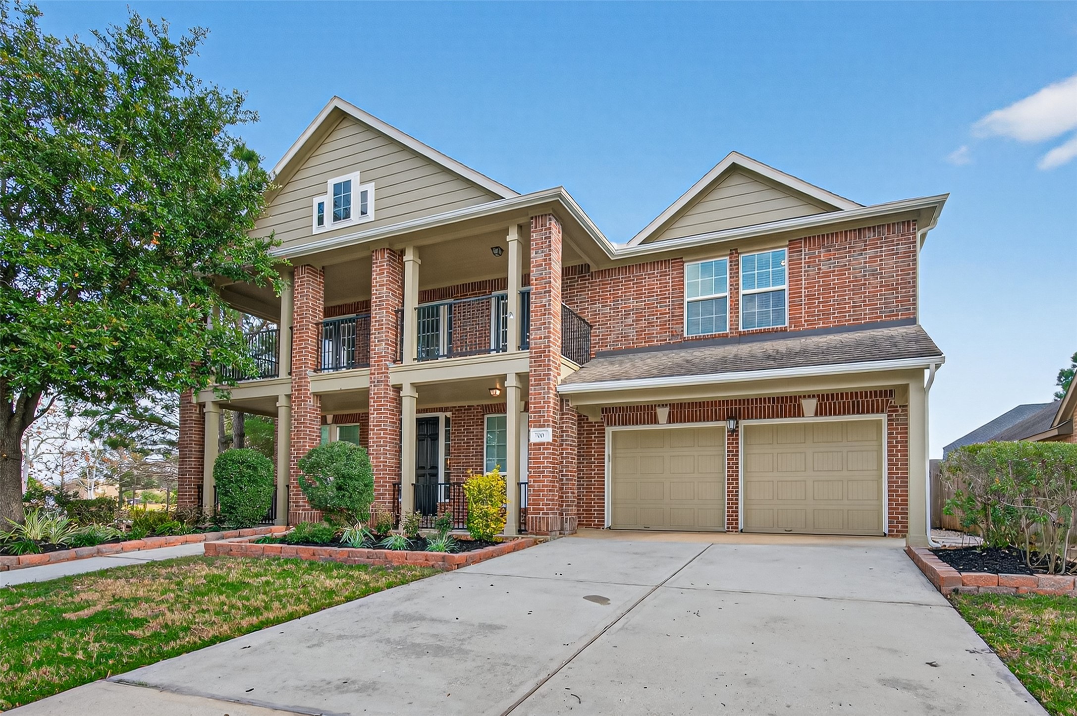 7003 Bristol Memorial Drive Spring, TX 77379 - Photo 2 of 40 Two-story brick home in Spring TX 77379 featuring covered front porch, upper balcony, and mature landscaping. This lake view home offers strong curb appeal with dual garage and extended driveway