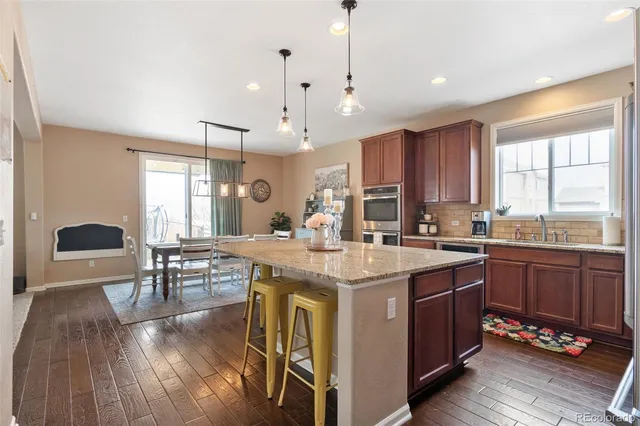 a kitchen with stainless steel appliances granite countertop a stove a sink dishwasher a dining table and chairs with wooden floor