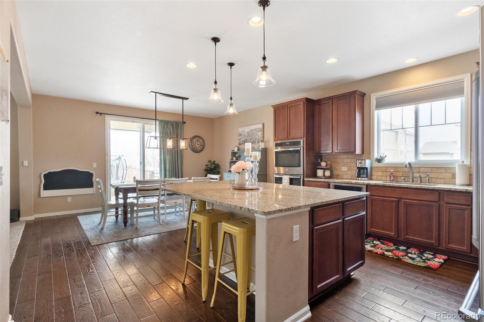 10995 Quintero Street Commerce City, CO 80022 - Photo 12 of 41 a kitchen with stainless steel appliances granite countertop a stove a sink dishwasher a dining table and chairs with wooden floor