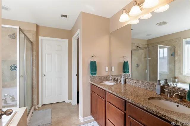 a bathroom with a granite countertop double vanity sink a mirror and a shower