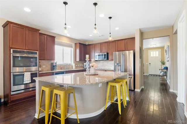a view of a kitchen with kitchen island a stove a refrigerator a sink and a dining table with wooden floor