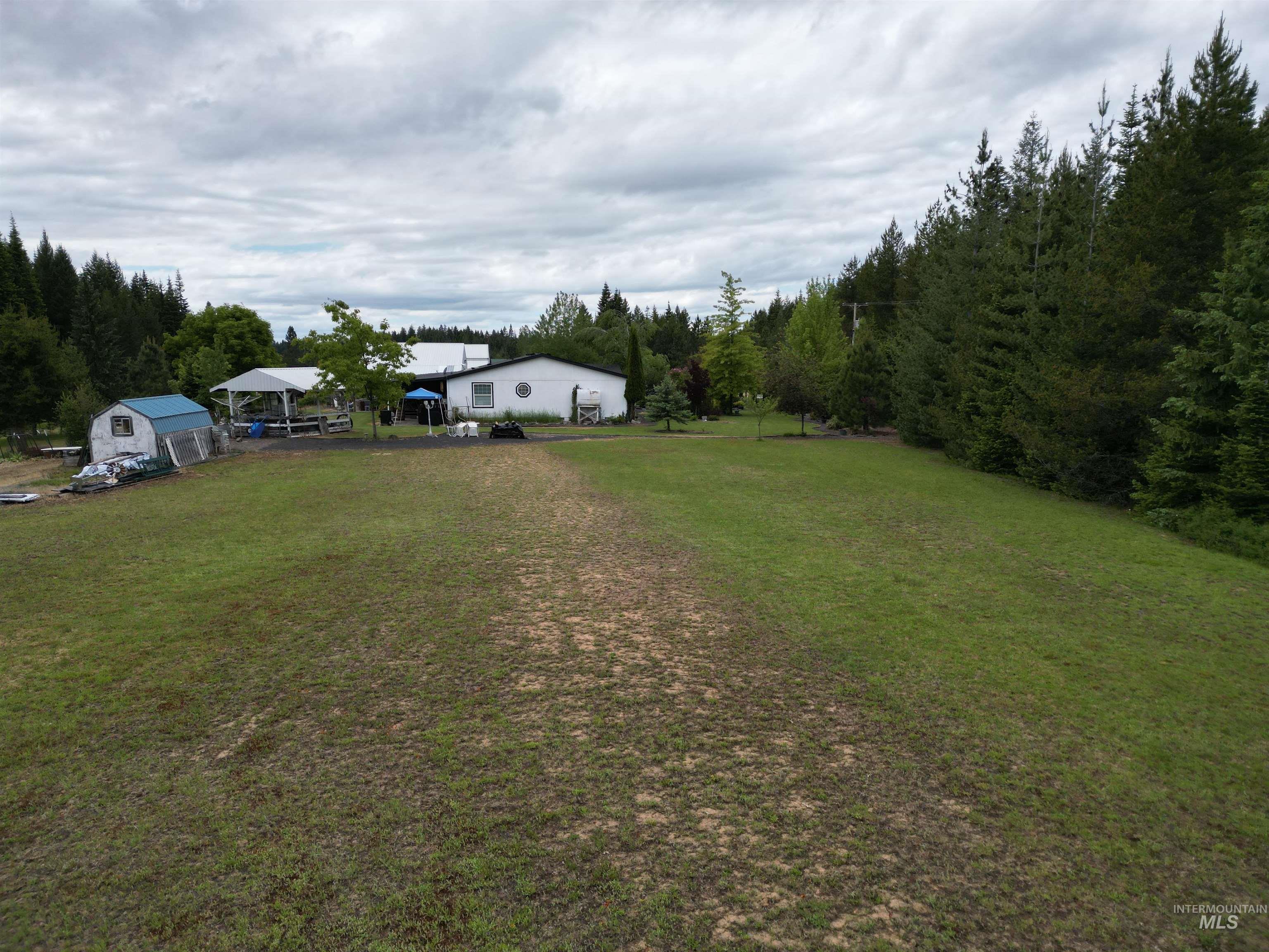 254 Lackey Road Weippe, ID 83553 - Photo 28 of 38 Expansive green lawn with a white residential structure, featuring a covered outdoor area and an adjacent outbuilding
