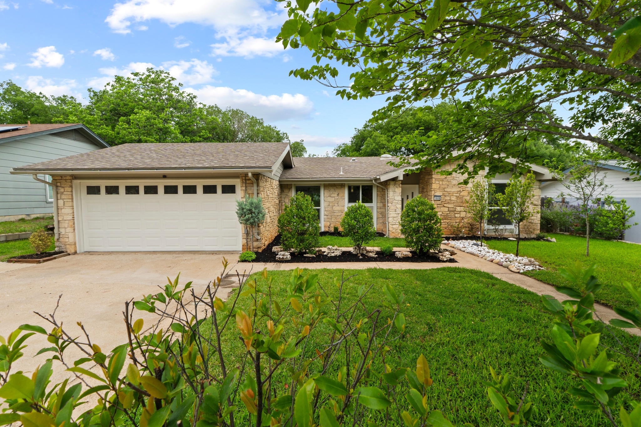 1608 Springer Lane Austin, TX 78758 - Photo 3 of 35 Stone facade residence featuring a two-car garage with paneling, a concrete driveway, and a flagstone pathway