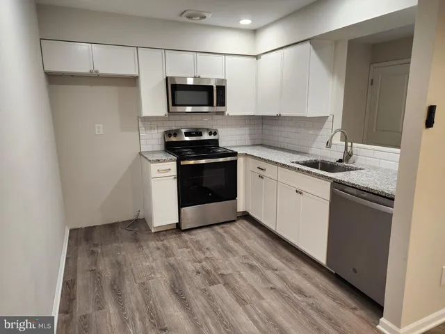 a kitchen with stainless steel appliances a sink dishwasher a refrigerator and a stove top oven with wooden floor