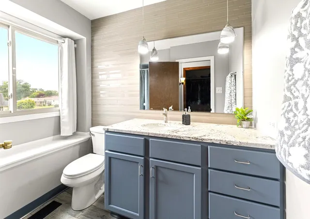 a bathroom with a granite countertop sink toilet mirror next to a window